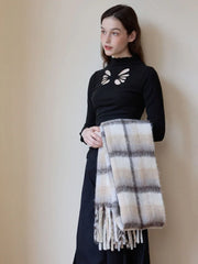 Close-up of a woman wearing a black mock-neck top with cut-out details, holding a folded plaid scarf with fringed edges.