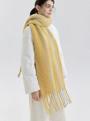 Woman wearing a yellow and gray striped scarf with fringe detail over a white puffer jacket, side view