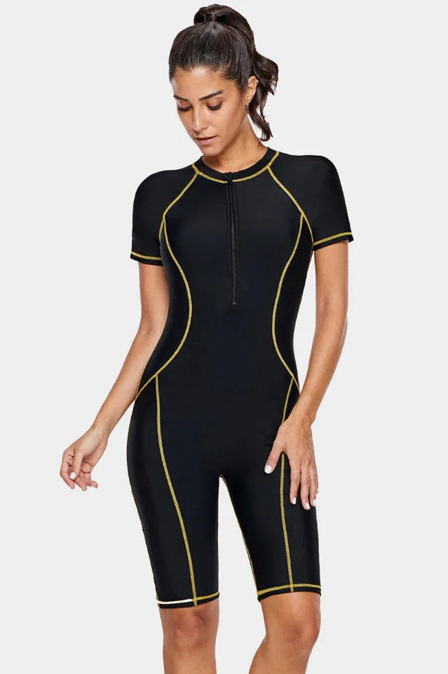 Woman wearing a black short-sleeve one-piece swimsuit with gold contrast stitching, front view