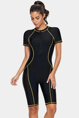 Woman wearing a black short-sleeve one-piece swimsuit with gold contrast stitching, front view