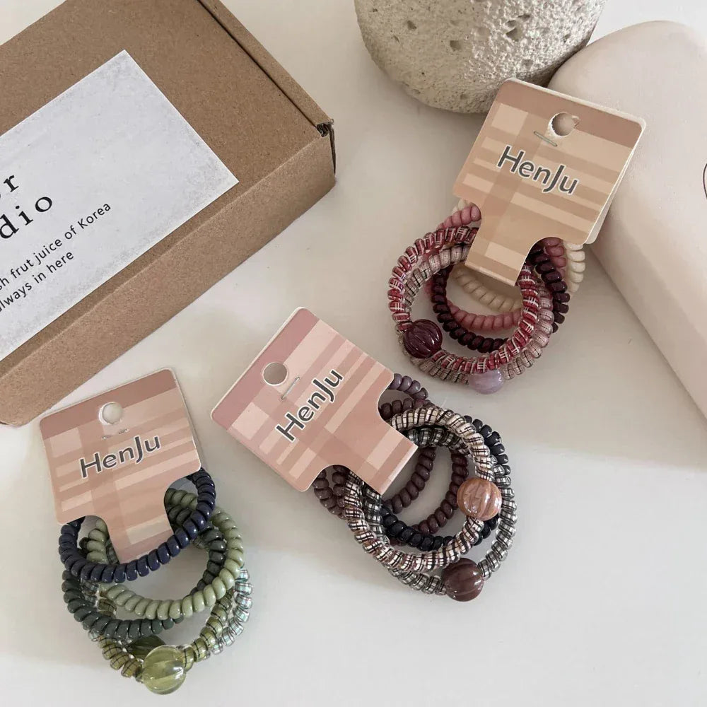 Several packs of spiral hair ties are laid out on a white surface next to a box and a cup.