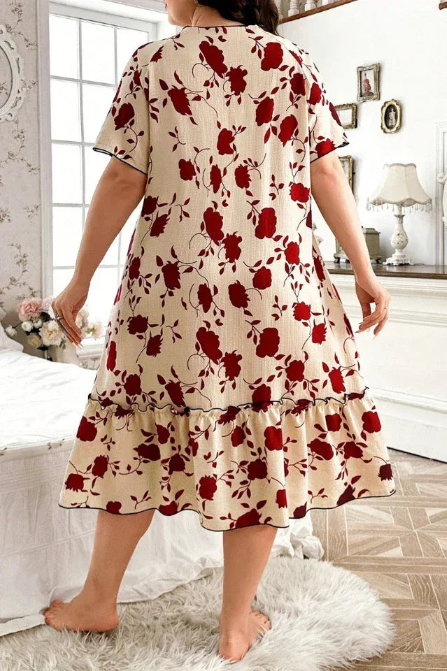 Plus size woman in a cream and red floral print short sleeve ruffled hem nightgown standing with her back to the camera in a bedroom.