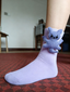 Close-up of a light purple ankle sock with a blue knitted bear embellishment attached to the cuff.