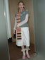 A woman stands wearing a gray sweater with lace sleeves, white shorts, pink shoes, and a striped scarf.
