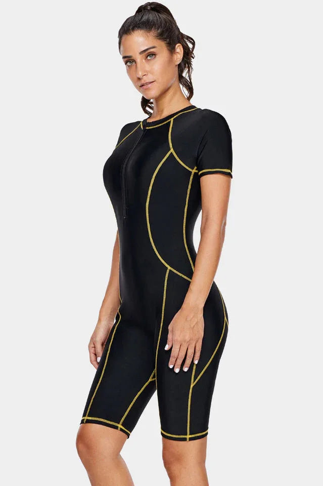 Woman wearing a black short-sleeve one-piece swimsuit with gold contrast stitching, side view