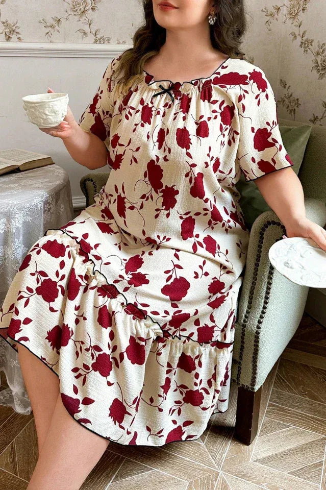 Plus size woman in a cream and red floral print short sleeve ruffled hem nightgown sitting in a chair holding a cup.