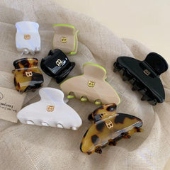 A collection of claw hair clips in various colors and patterns arranged on a textured fabric.