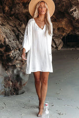 Woman wearing a white bohemian-style dress with lace sleeves and a straw hat on a beach