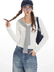 Model posing with a white long-sleeved top with striped trim and wide-leg blue jeans, holding a navy handbag and wearing a navy baseball cap.