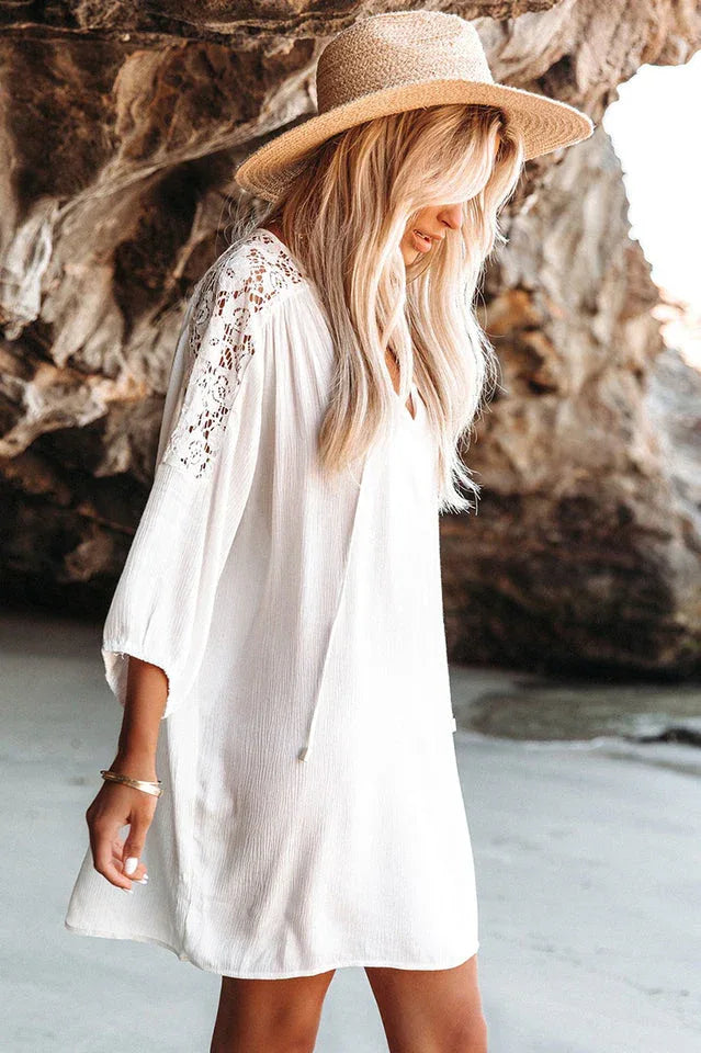 Woman in a white bohemian-style dress with lace sleeves and a straw hat walking on a beach