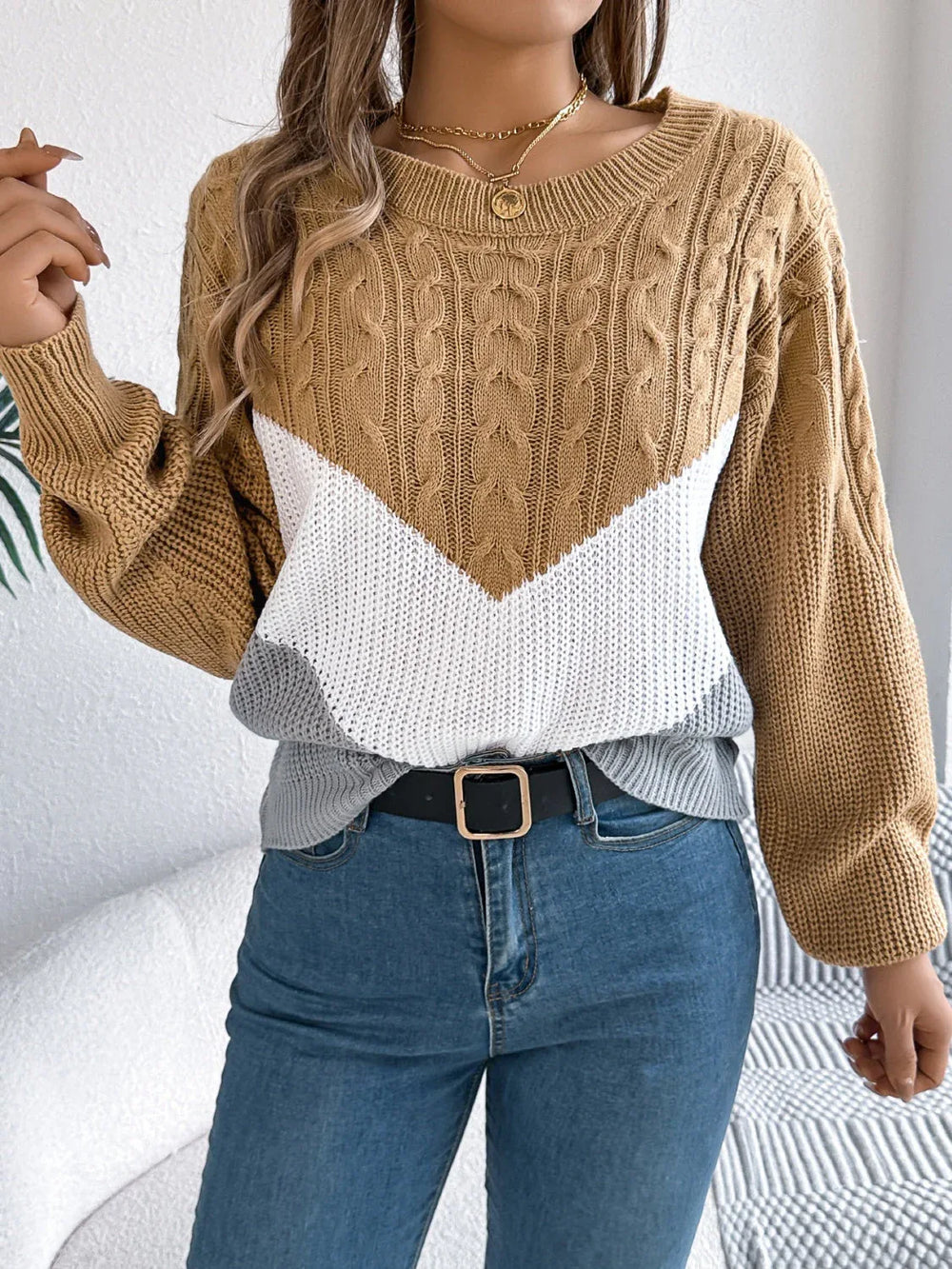 Woman wearing a brown, white, and grey colorblock chevron knit sweater with blue jeans and a black belt