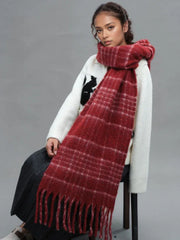 A woman is sitting while wearing a white sweater and a prominent red plaid scarf with fringe.