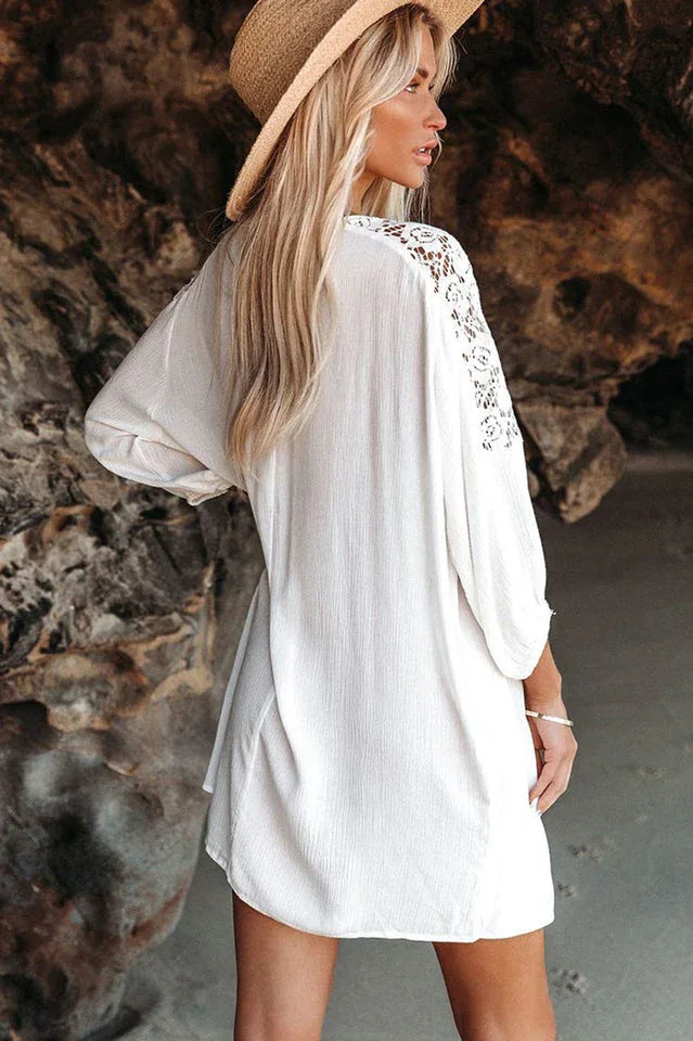 Back view of a woman wearing a white bohemian-style dress with lace sleeves and a straw hat