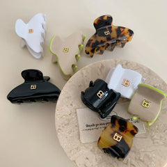 A selection of claw hair clips in different colors and styles, including tortoiseshell, white, black, and beige, arranged on a marble-like surface with fabric.