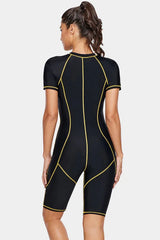Woman wearing a black short-sleeve one-piece swimsuit with gold contrast stitching, back view