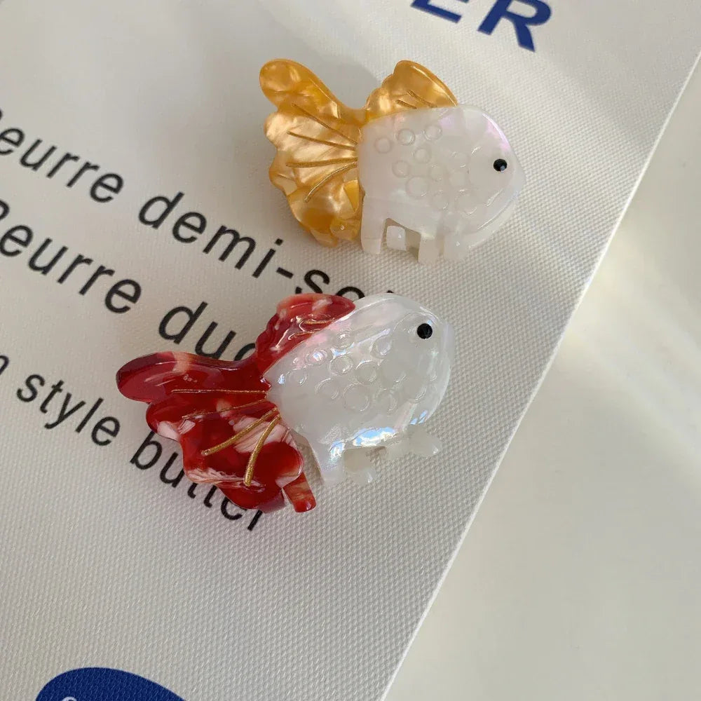 Two goldfish hair clips, one orange and white, one red and white, on a white surface