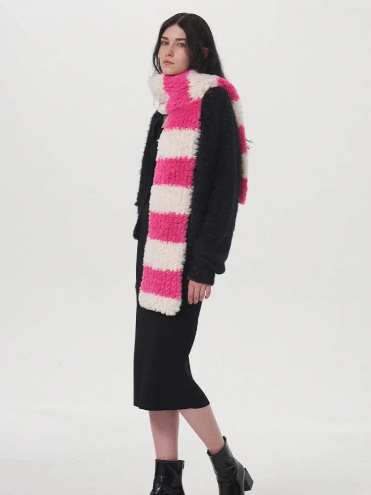 Side view of a model wearing a black sweater, black dress, and a pink and white striped fuzzy scarf.