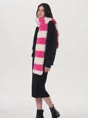 Side view of a model wearing a black sweater, black dress, and a pink and white striped fuzzy scarf.
