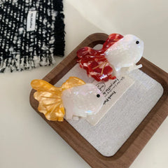 Two goldfish hair clips, one orange and white, one red and white, on a wooden tray