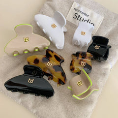 A variety of claw hair clips in tortoiseshell, white, black, and beige with lime green trim, displayed on a neutral fabric.