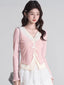 Woman wearing a pink V-neck knit cardigan with lace trim and bow closures over a cream-colored top and a white polka dot ruffled skirt.