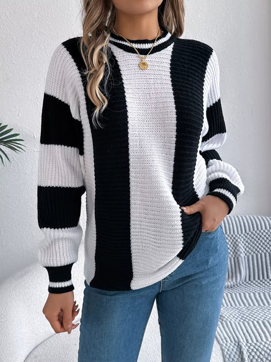 Woman wearing a black and white striped knit sweater with blue jeans and a gold necklace, front view.