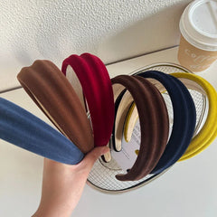 Assortment of velvet padded headbands in various colors including blue, brown, red, navy, and yellow, held in a hand