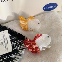 Close-up of two goldfish hair clips, one orange and white, one red and white, on a white cloth