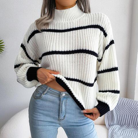 Woman wearing a white and black striped knit sweater with a high neckline and long sleeves, paired with light blue jeans.