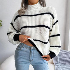 Woman wearing a white and black striped knit sweater with a high neckline and long sleeves, paired with light blue jeans.