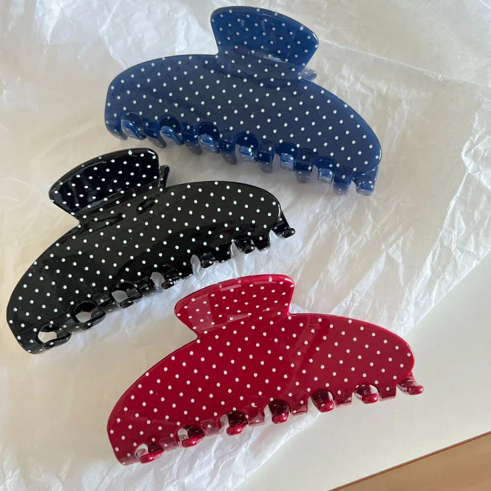 Three polka dot hair claw clips in blue, black, and red on white textured paper