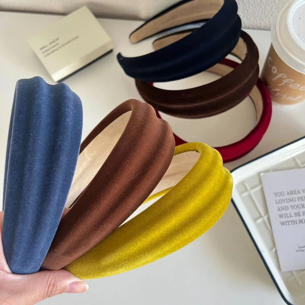 Close-up of velvet padded headbands in blue, brown, and yellow, with other colors blurred in the background