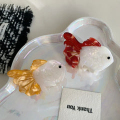 Two goldfish hair clips, one orange and white, one red and white, on a pearlescent dish