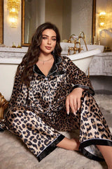 Woman wearing a leopard print satin pajama set, sitting on a rug in front of a bathtub.