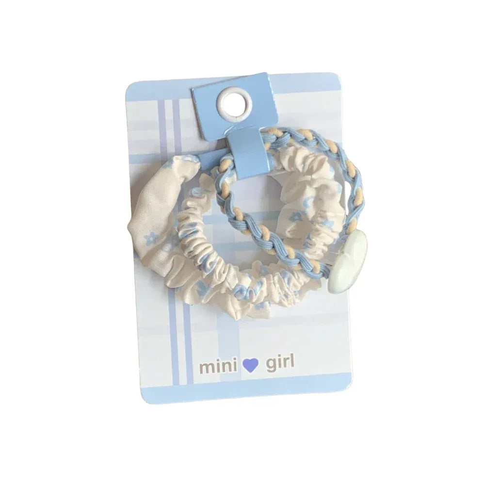 Set of two blue and white floral print scrunchies with braided accents on a light blue striped card
