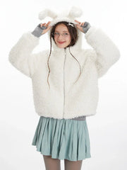 Front view of a model wearing a white fuzzy hooded jacket with bunny ears, a grey turtleneck, and a light blue pleated skirt. She is posing with her hands near the hood.