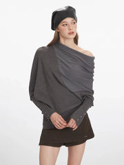 Woman adjusting the draped neckline of her grey asymmetrical knit sweater.
