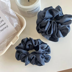 Two denim scrunchies next to a candle and a basket