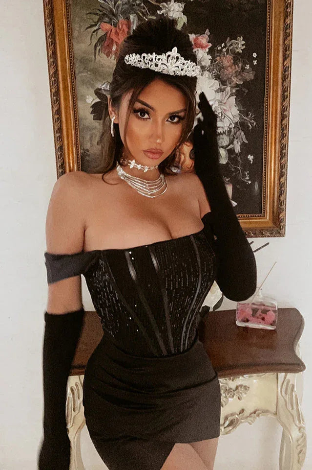 Woman wearing a black off-the-shoulder sequin and satin dress with a tiara and gloves