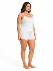 Side profile of a woman wearing a white ribbed camisole and shorts pajama set with pink lace trim.