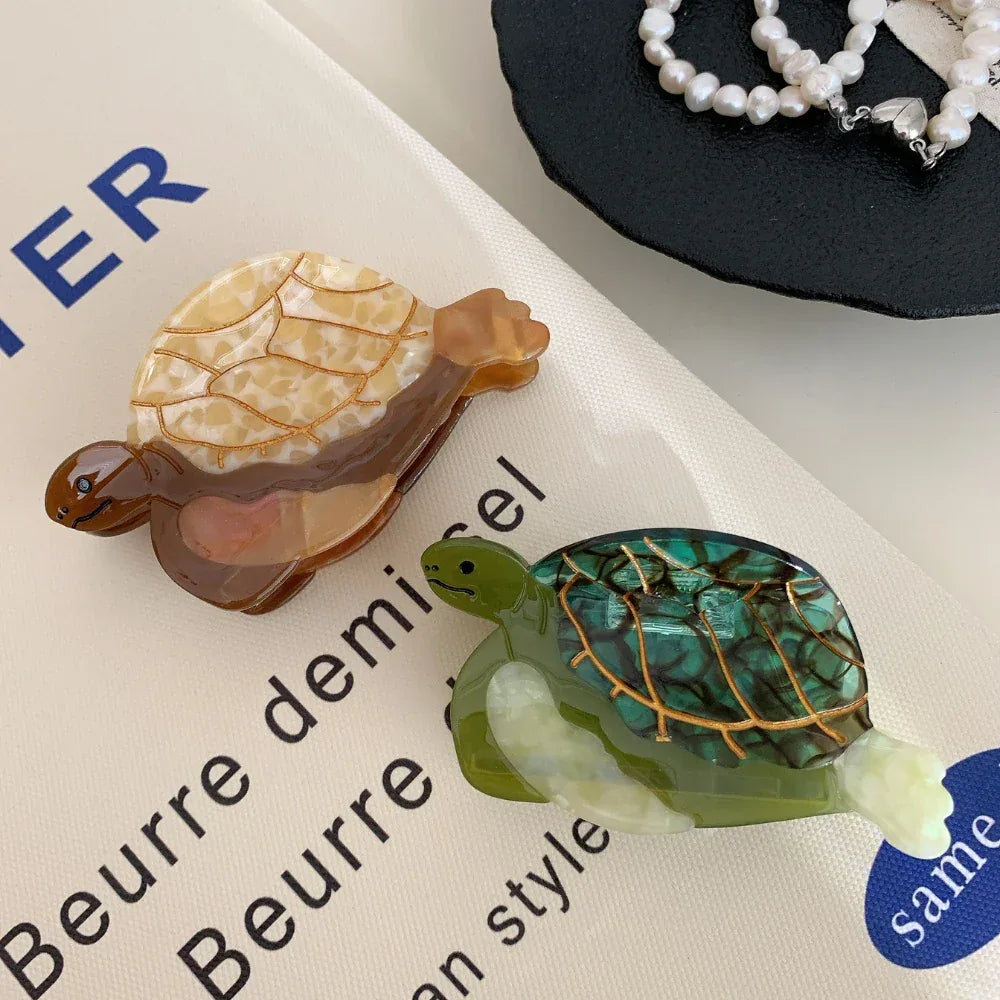 Top-down view of two acetate turtle hair clips, green and brown/tan, placed on a white surface with French text