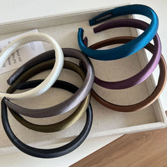 Assorted padded satin headbands in a tray, showing multiple colors including white, grey, olive green, black, purple, teal, and brown