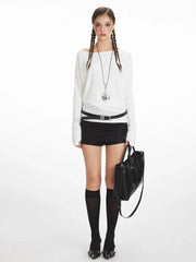 Model wearing a white off-the-shoulder long-sleeve top, black high-waisted shorts, black knee-high socks, and black heels, holding a black tote bag.