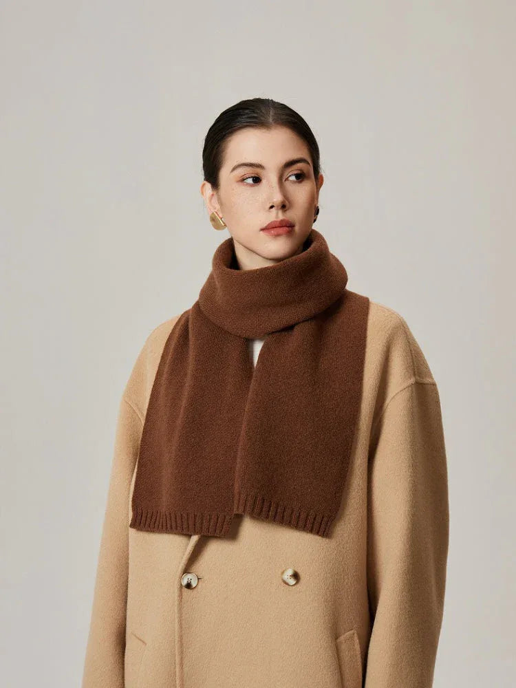 Woman wearing a brown knit scarf and a tan coat.