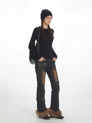 Model from the side wearing a black ribbed knit top, distressed flared jeans with fur trim cuffs, and a black beanie, with the fringe detail bag slung over the shoulder.