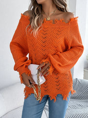 Woman holding a white clutch while wearing an orange distressed off-the-shoulder knit sweater and blue jeans.