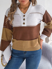 Front view of a woman wearing a brown, tan, and white color block knit sweater with a v-neck and button details, paired with blue jeans and holding a white clutch.