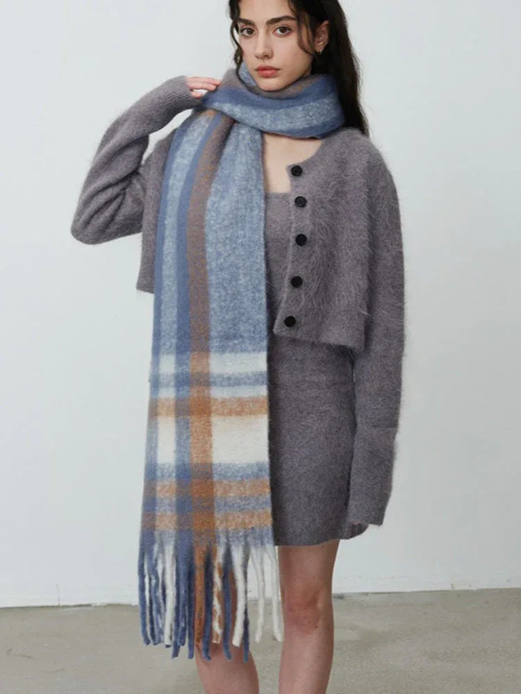 Woman adjusting her plaid scarf over a grey knit dress and cardigan