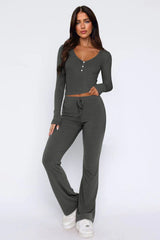 Woman wearing a charcoal ribbed knit long-sleeve top with button detail and matching flared pants, front view.