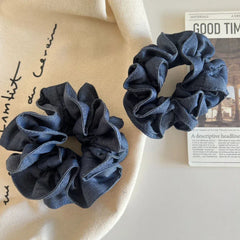 Two denim scrunchies on a beige cloth next to a newspaper